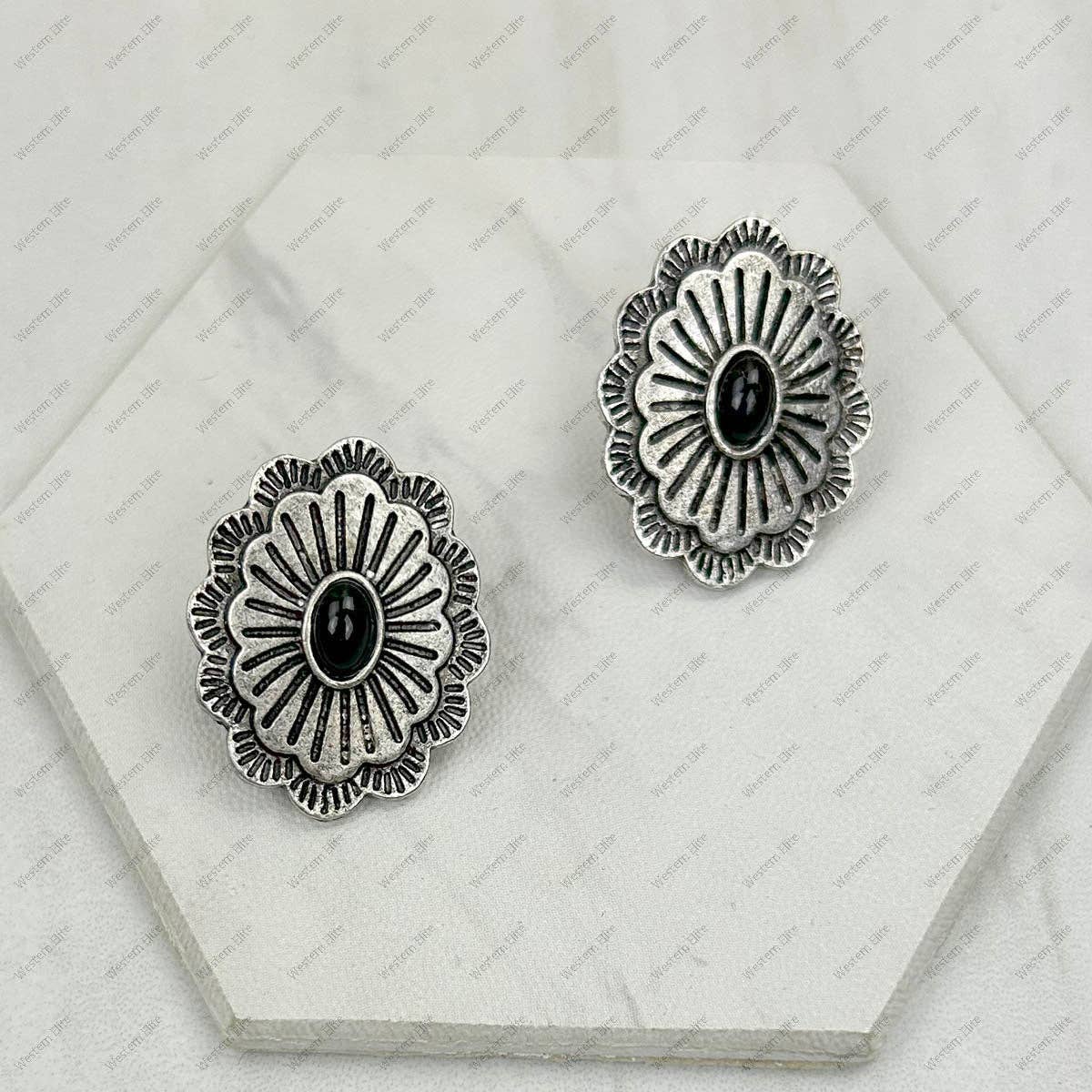 Pair of silver floral earrings with black centers on a white hexagonal display stand.