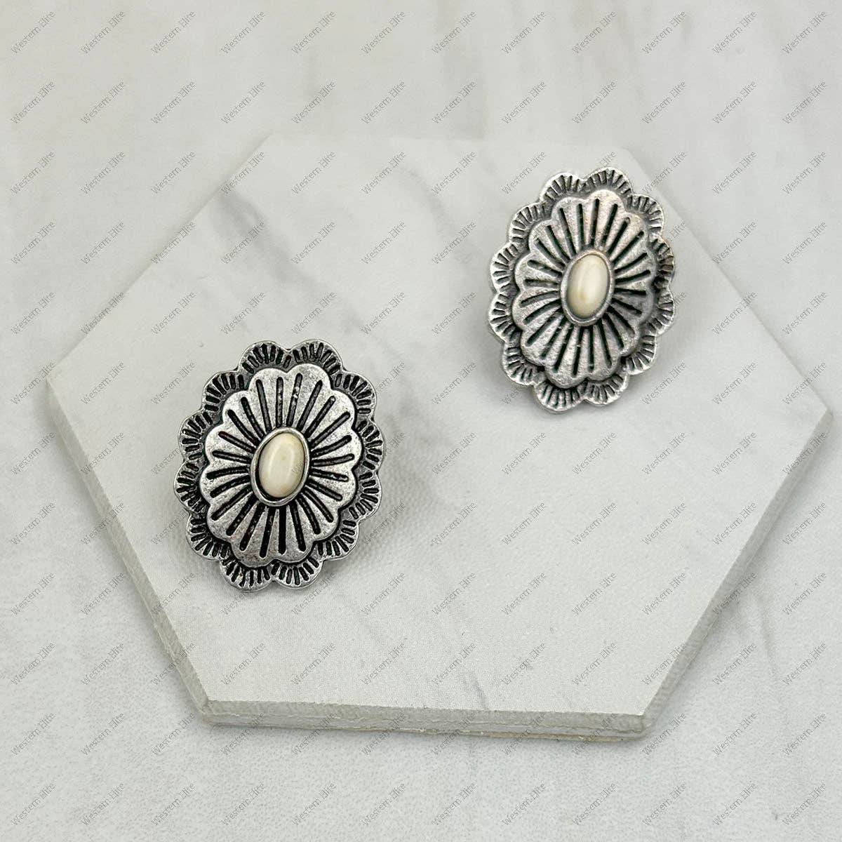 Pair of silver floral earrings with central stones on a hexagonal stone surface.