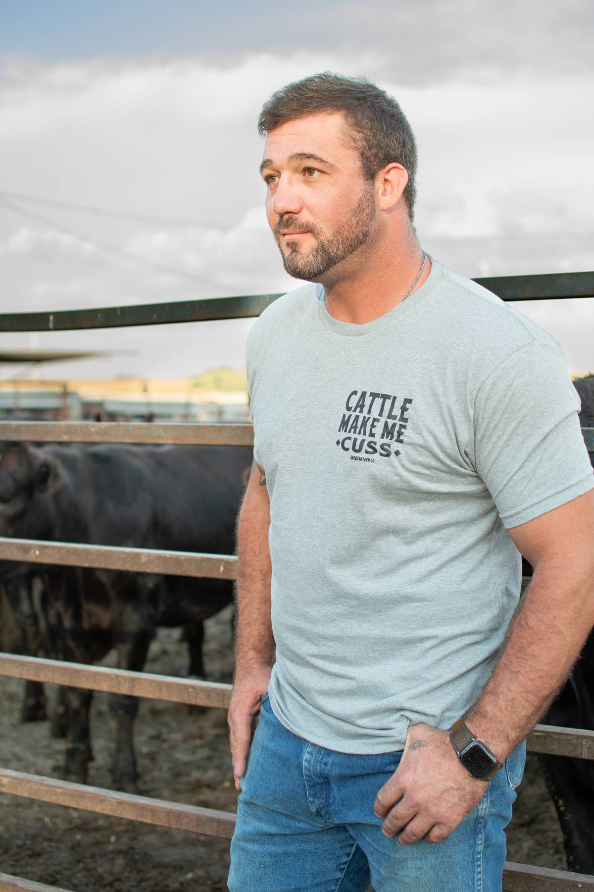 Man wearing a light blue t-shirt with text standing in front of a fence with cows.