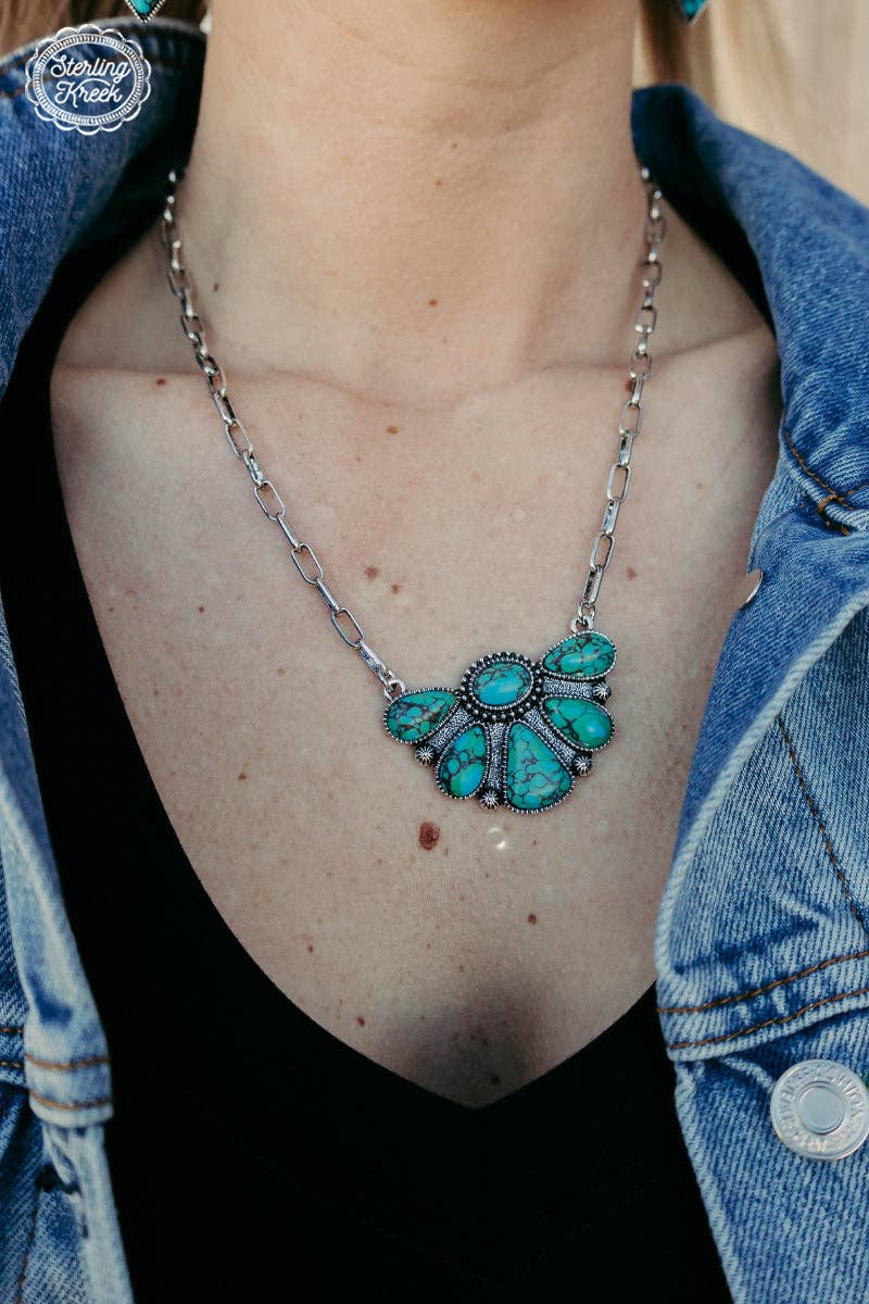 Turquoise necklace with silver chain on a person wearing a denim jacket.