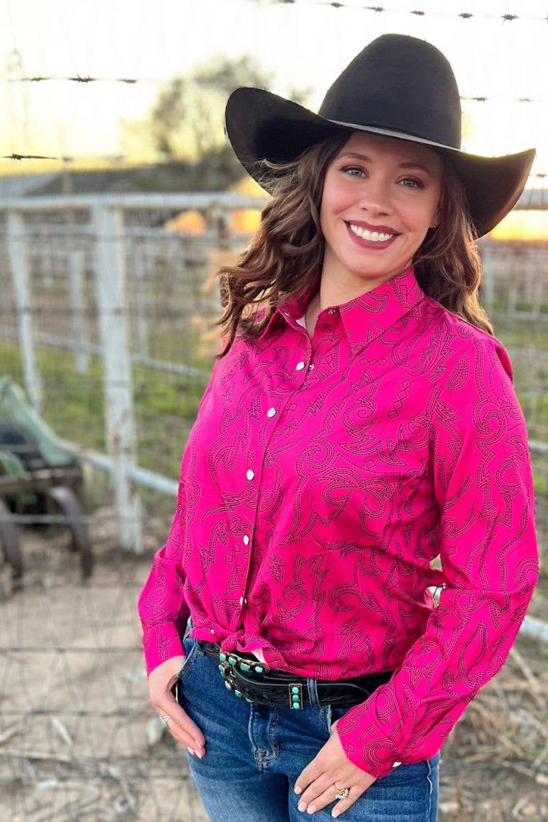 Woman wearing a pink patterned shirt, blue jeans, and a black cowboy hat outdoors.