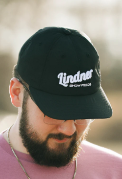 Man wearing a black cap with 'Lindner' logo, blurred background