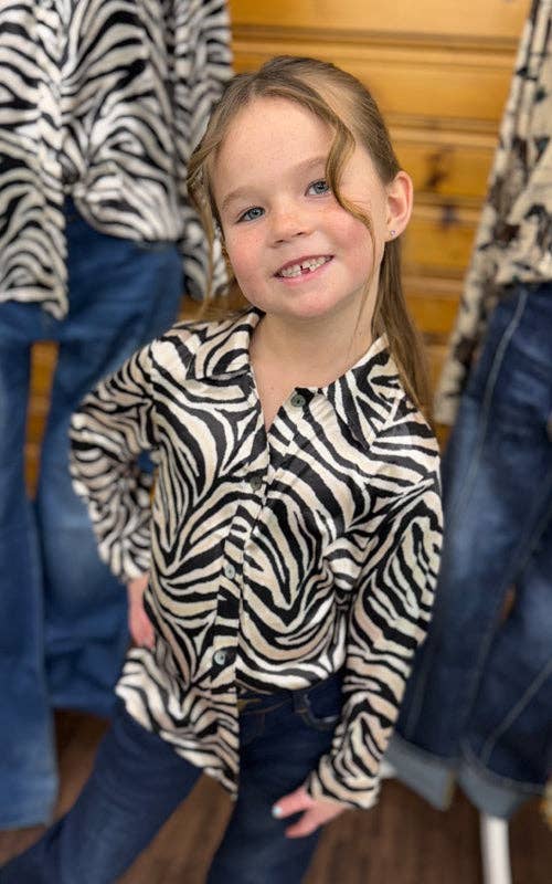 Child wearing a zebra print shirt standing in front of clothing racks.