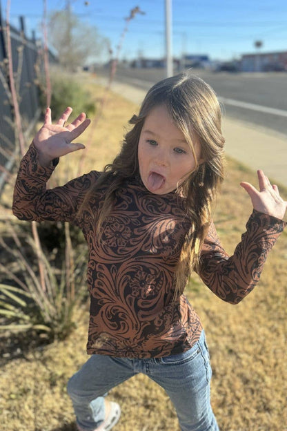 Child wearing a patterned long-sleeve shirt and jeans outdoors on a sunny day.