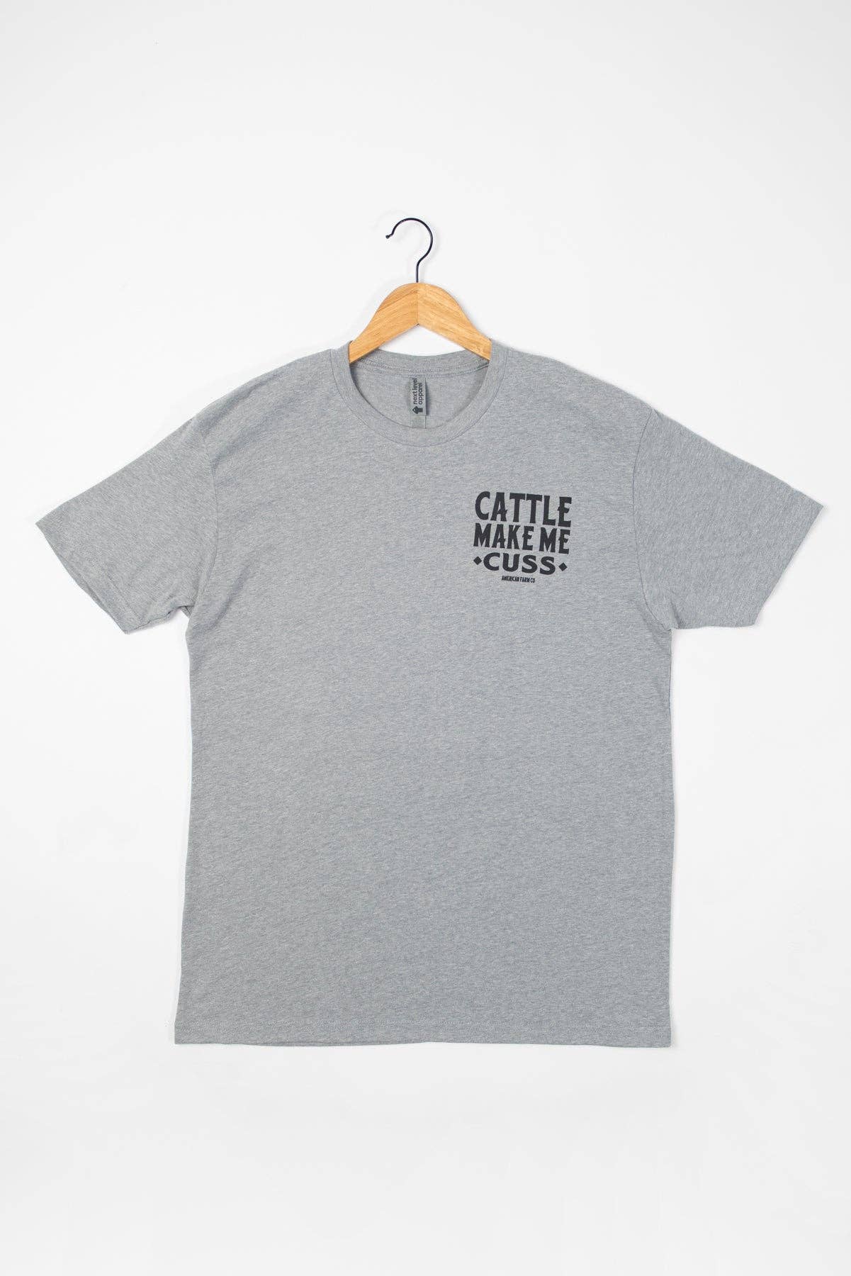 Gray t-shirt with 'Cattle Make Me Cuss' text on a hanger against a white background