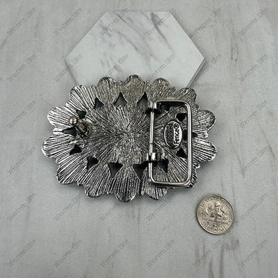 Decorative silver belt buckle on a marble surface with a coin for scale.
