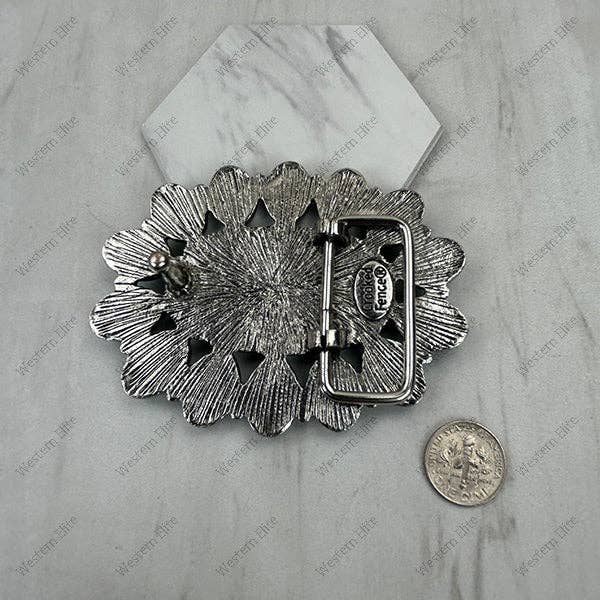 Decorative silver belt buckle on a marble surface with a coin for scale.