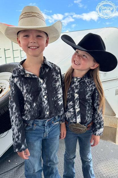 Two children in cowboy hats and matching shirts standing outdoors.