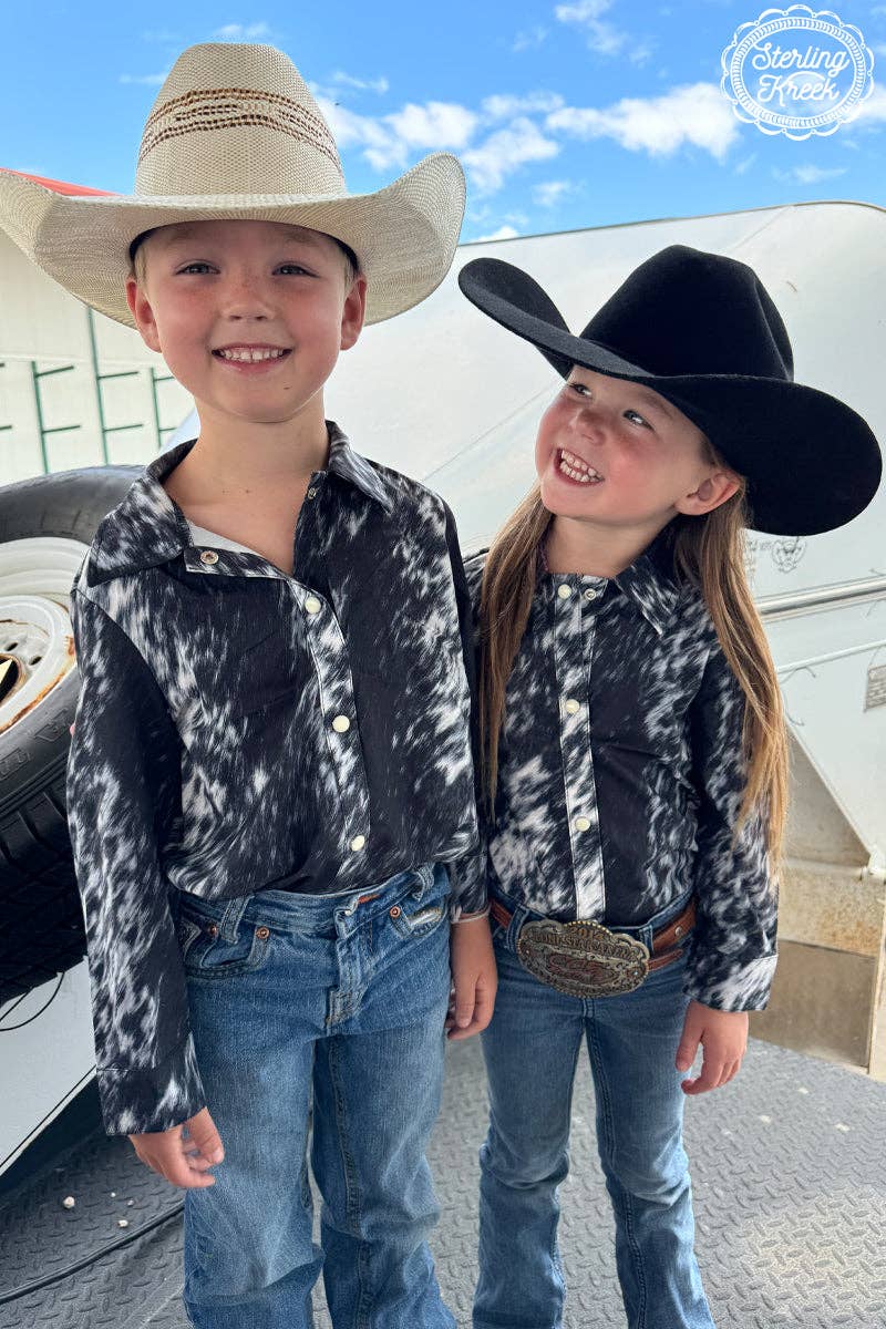 Two children in cowboy hats and matching shirts standing outdoors.