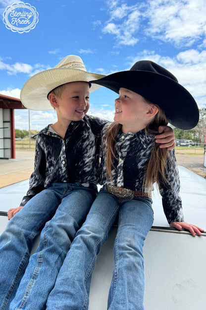 Two children wearing cowboy hats sitting on a vehicle with a clear blue sky in the background.