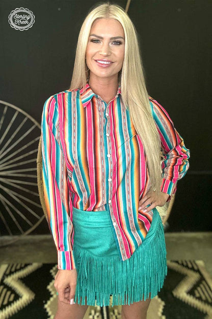 Woman wearing a colorful striped shirt and turquoise fringed skirt on a patterned background