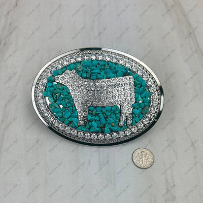 Decorative belt buckle with turquoise stone inlay and silver cow design, size comparison with a coin shown.