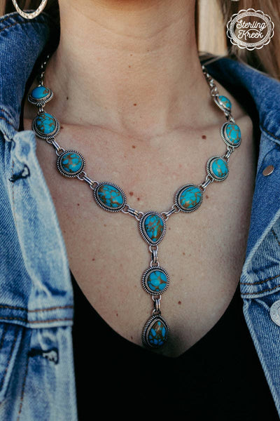 Turquoise necklace worn by a person with a denim jacket, brand 'Caring Creek' visible.