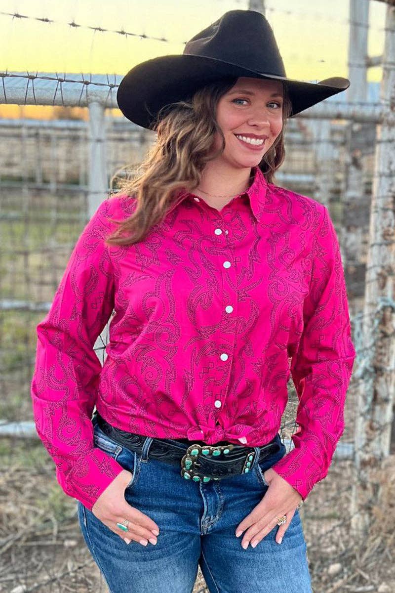 Woman wearing a pink patterned shirt, blue jeans, and a black cowboy hat outdoors.
