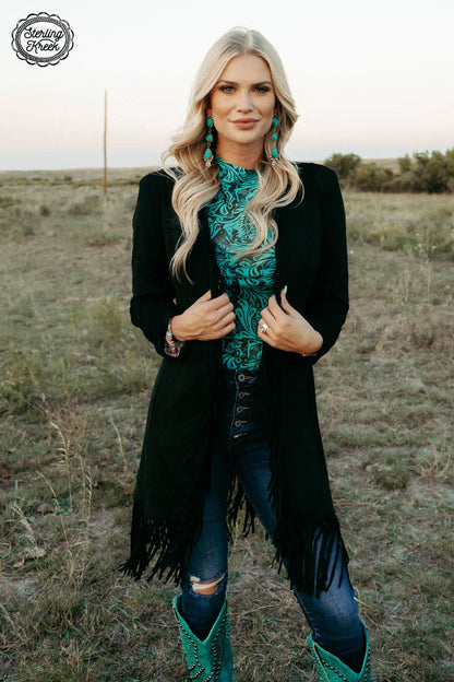Woman in a black fringe coat and teal outfit standing in a field