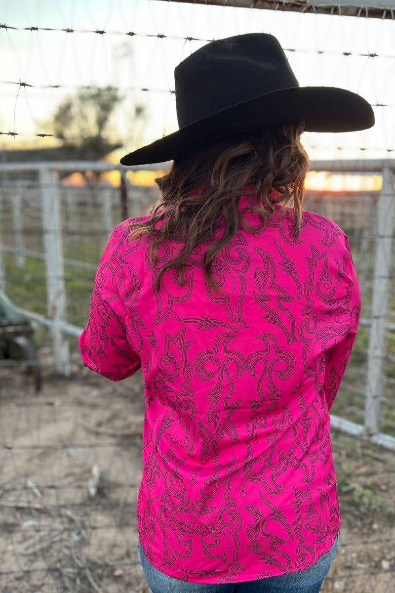 Person wearing a bright pink long-sleeve shirt with black patterns and a black cowboy hat, standing in front of a barbed wire fence.