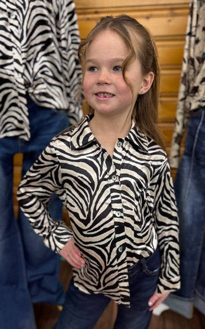 Child wearing a zebra-patterned shirt standing in front of zebra-patterned clothing racks.