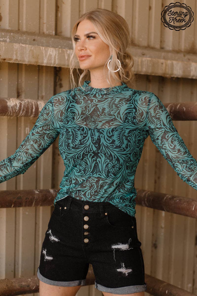 Woman wearing a teal lace top and black shorts in front of wooden stalls.
