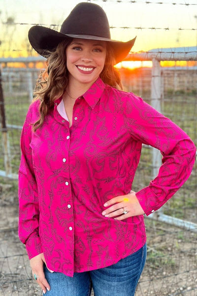 Woman wearing a pink patterned shirt and black cowboy hat with a sunset in the background.