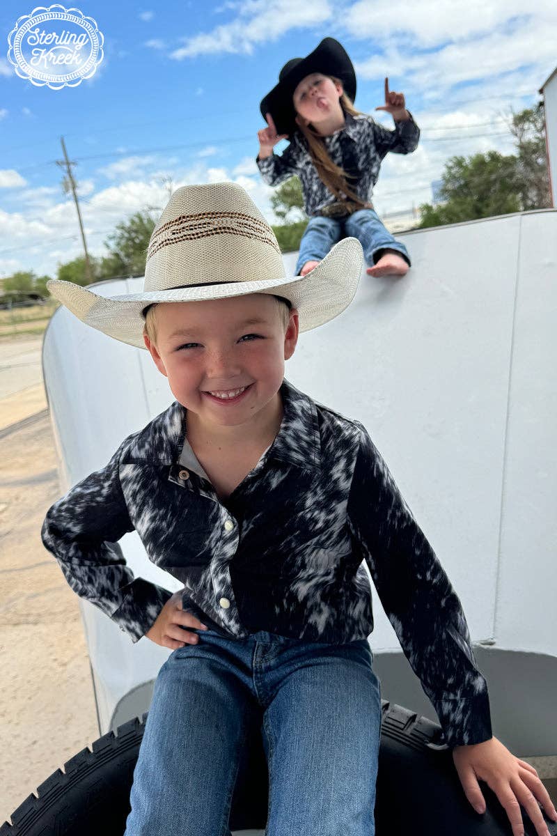 Two children in cowboy hats sitting on a truck bed with a clear sky and trees in the background.
