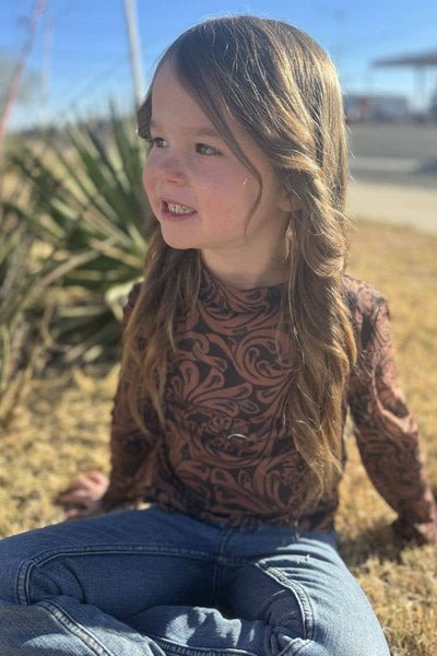 Young girl sitting outdoors with a patterned shirt and jeans