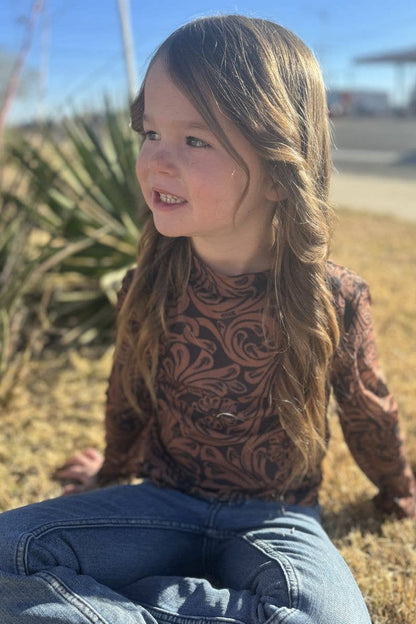Young girl sitting outdoors with a patterned shirt and jeans