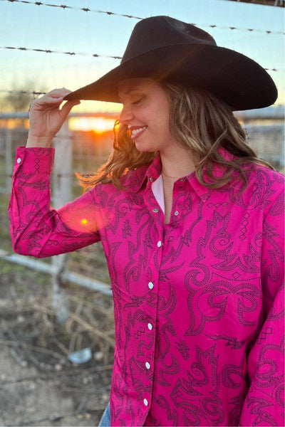 Woman wearing a pink patterned shirt and brown cowboy hat with a sunset in the background.