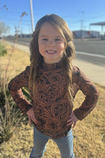 Young girl wearing a patterned long-sleeve shirt outdoors on a sunny day.