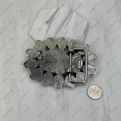 Silver floral-patterned belt buckle on a marble surface with a coin for scale.