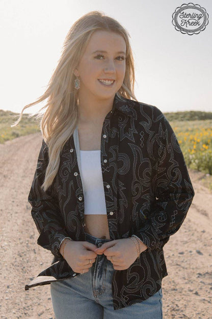 Woman wearing a black patterned shirt outdoors with a clear sky.