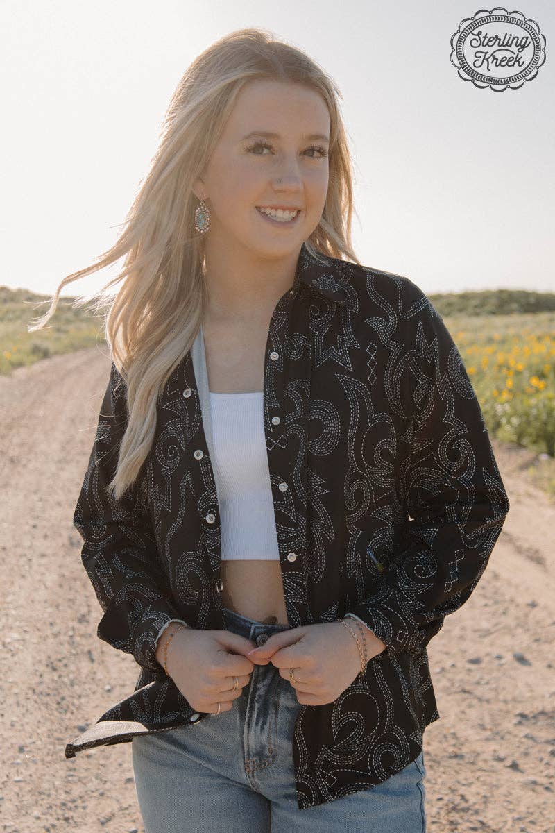 Woman wearing a black patterned shirt outdoors with a clear sky.