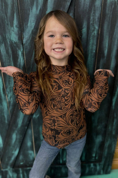 Child wearing a patterned shirt standing against a dark curtain