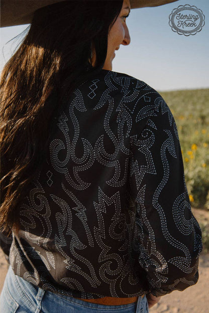 Person wearing a black patterned shirt with a blurred natural background
